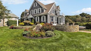 A large, two-story house with a prominent front porch, stone foundation, and a well-maintained garden. - Offers  ocean Views and Access & is Great for All Ages! (2249) (West Yarmouth)