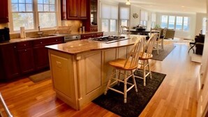 A spacious kitchen with a large island, wooden cabinets, and a dining area with chairs. - Offers  ocean Views and Access & is Great for All Ages! (2249) (West Yarmouth)