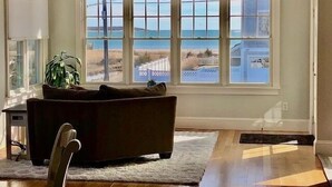 A living room with a large window overlooking a beach and a house. - Offers  ocean Views and Access & is Great for All Ages! (2249) (West Yarmouth)