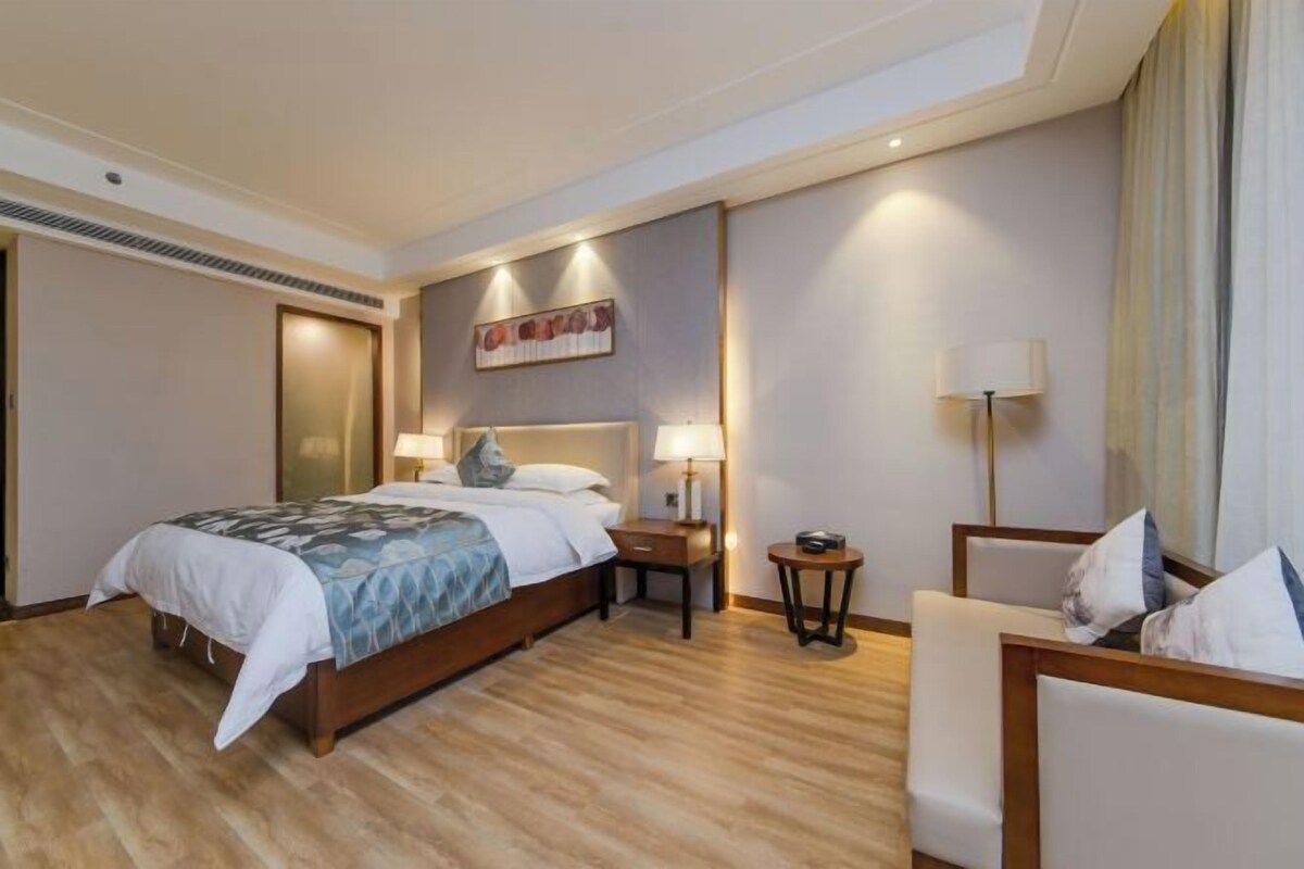 Ein Hotelzimmer mit einem großen Bett, Nachttischen, einem Sessel und einem Bild an der Wand.