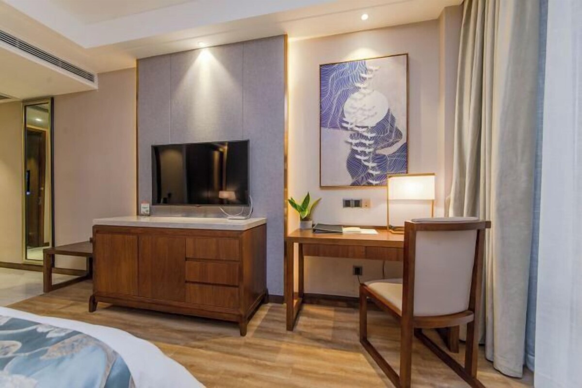 Ein Hotelzimmer mit einem Holztisch, einem Fernseher, einem gerahmten Kunstwerk und einem Bett.