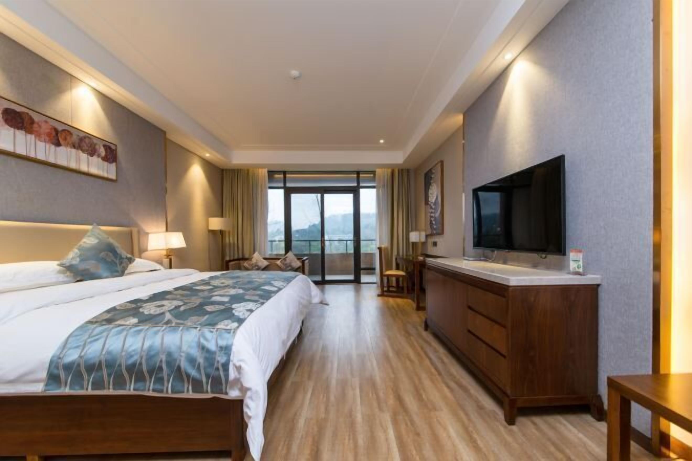 A hotel room with a large bed, a TV, a wooden dresser, and a balcony with a view.