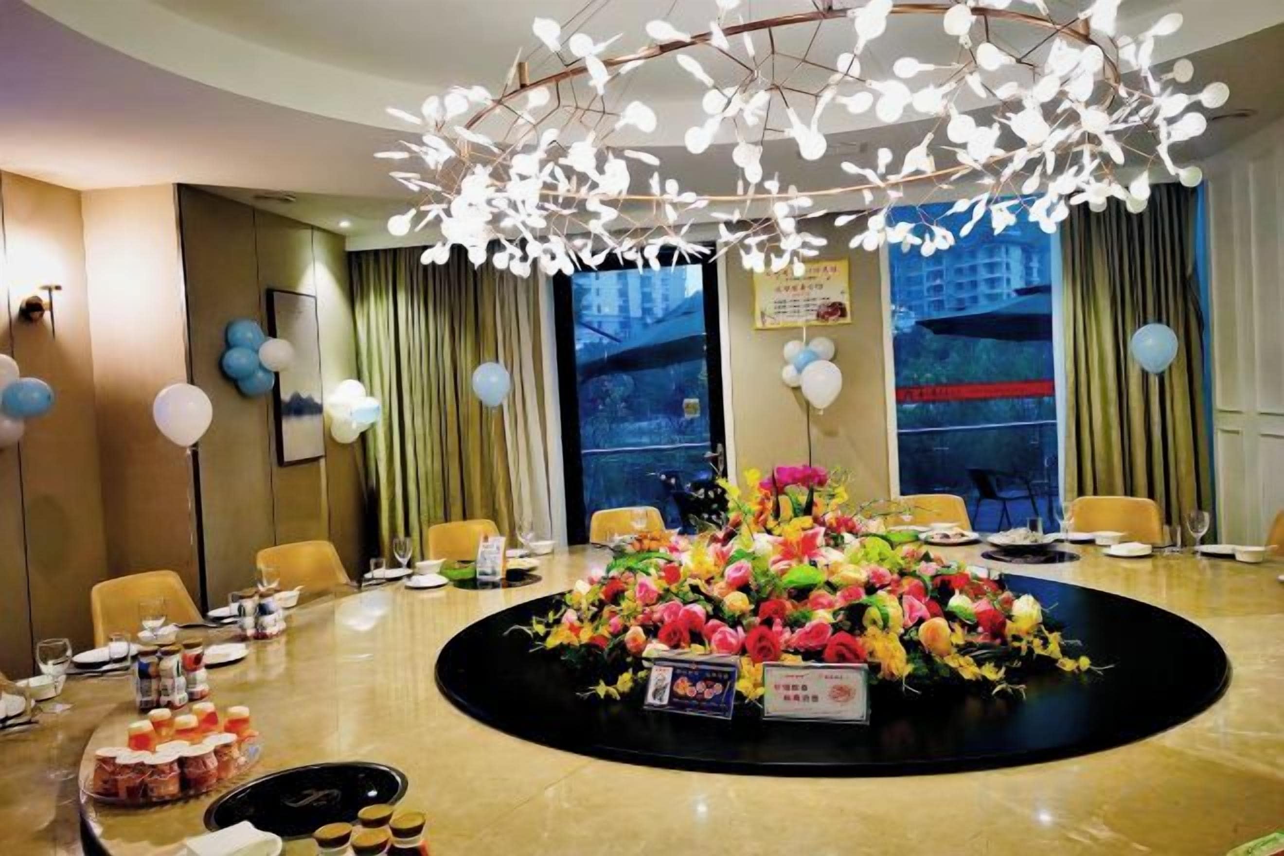 A hotel conference room with a round table, chairs, a floral centerpiece, and a modern chandelier.