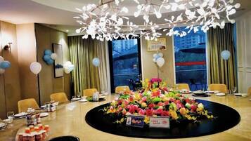 A hotel conference room with a round table, chairs, a floral centerpiece, and a modern chandelier.