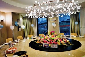 A hotel conference room with a round table, chairs, a floral centerpiece, and a modern chandelier. - Huatian Hotel (Jiahe)