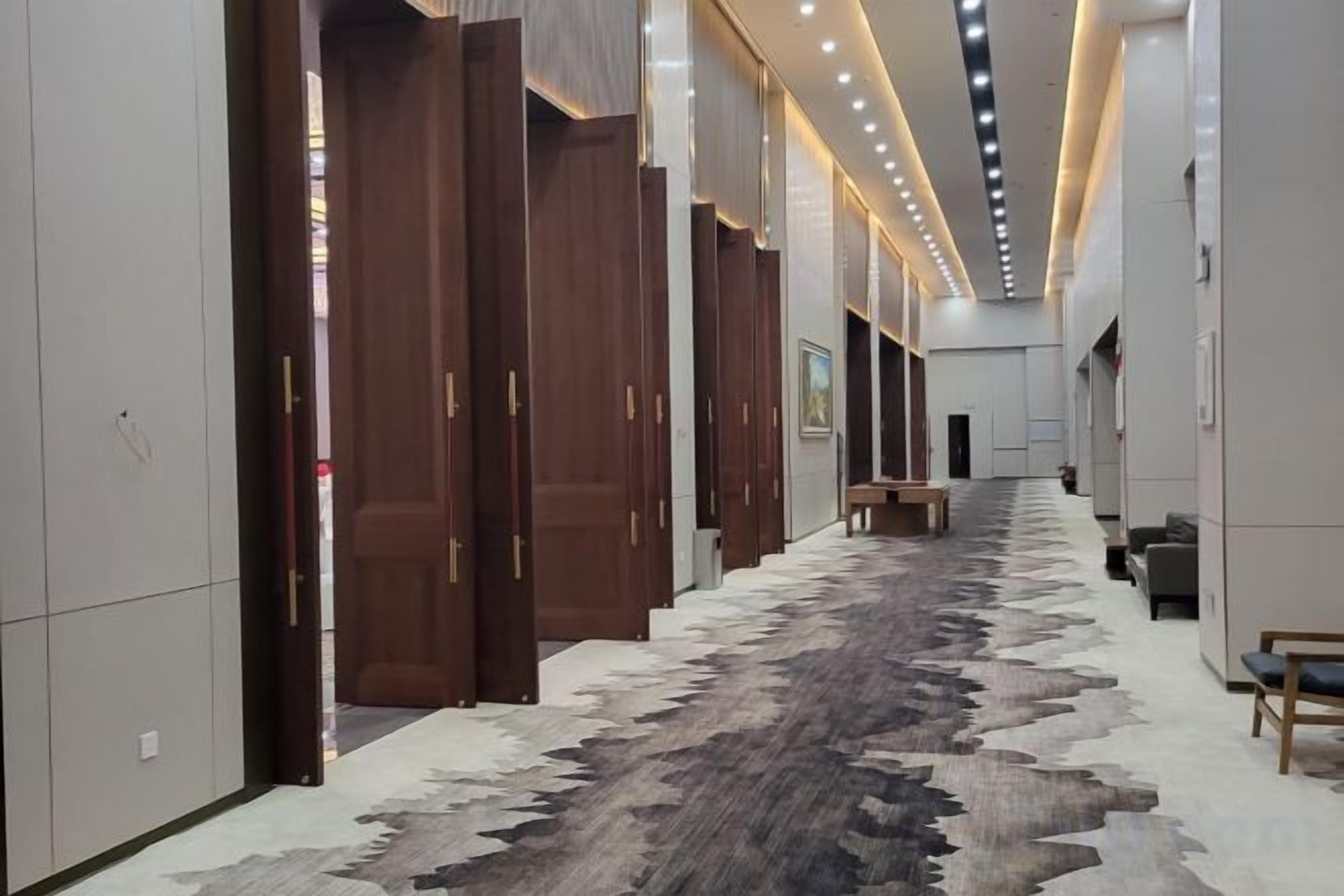 A hallway with wooden doors, a patterned carpet, and a bench.