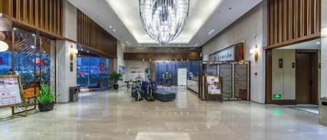 A spacious lobby with a modern chandelier, seating areas, and a reception desk.