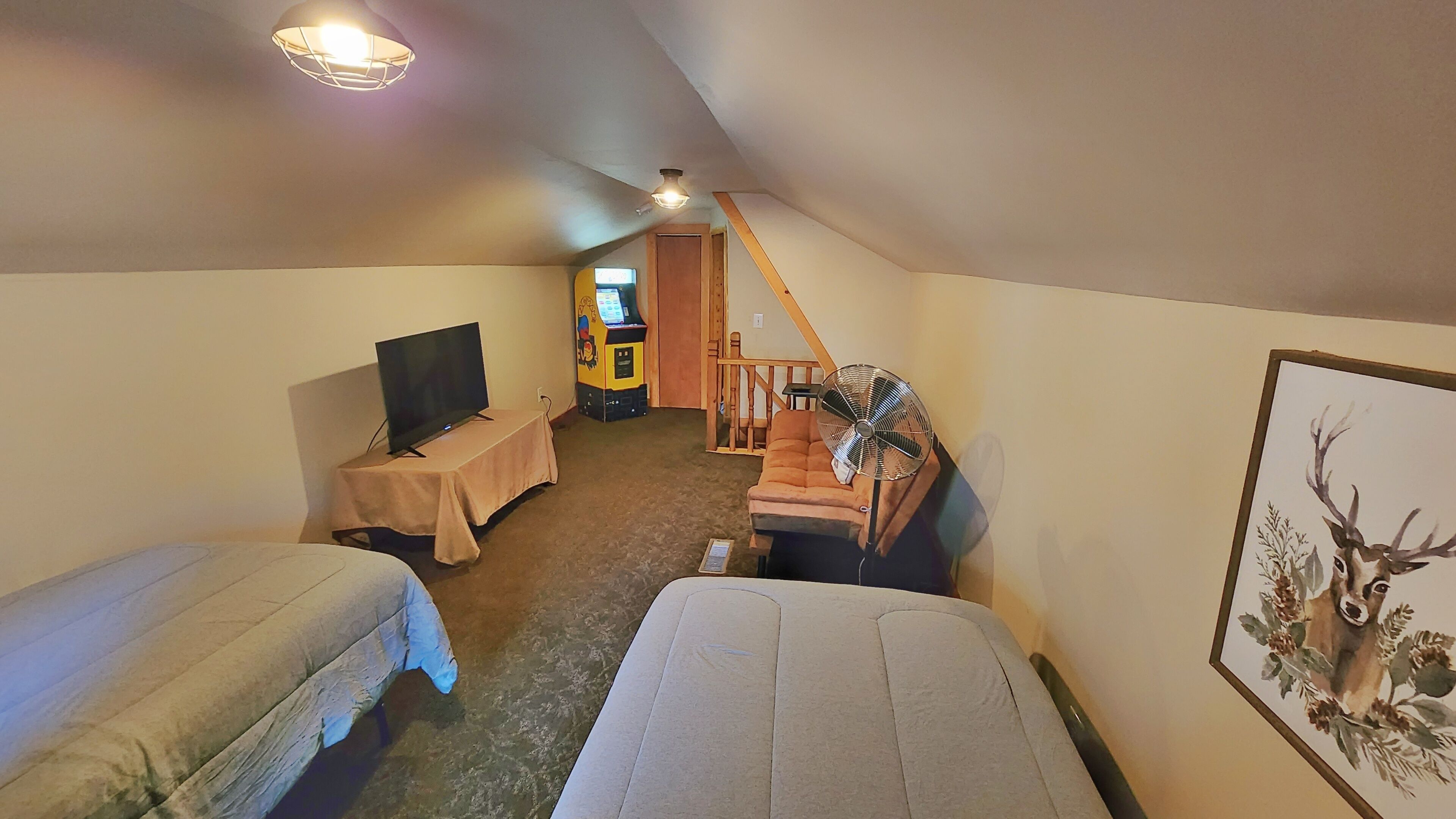 A small, cozy room with two beds, a television, a fan, and a painting on the wall.