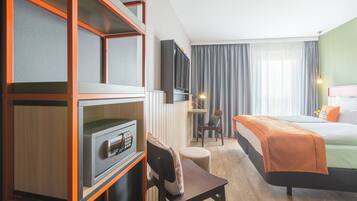 A hotel room with a bed, a desk with a chair, a TV, and a minibar.