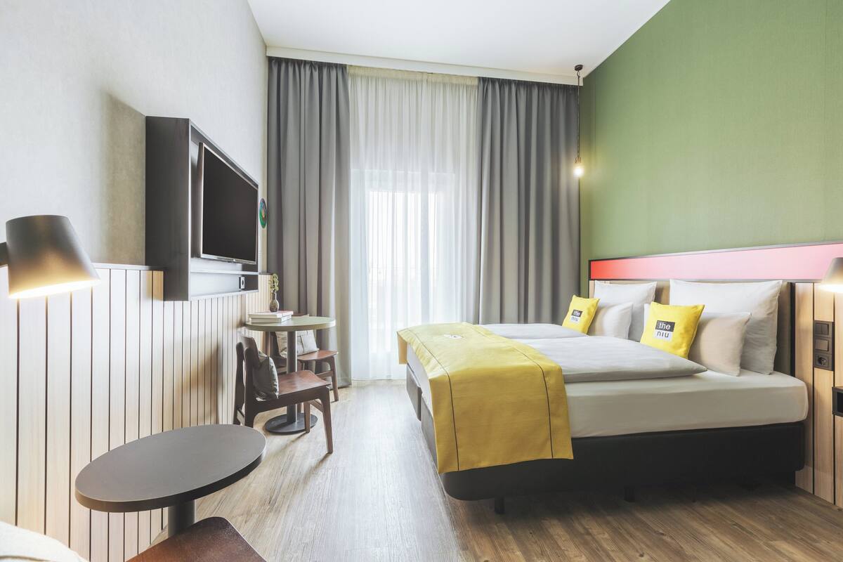 A hotel room with a bed, a TV mounted on the wall, a small table, and a chair.