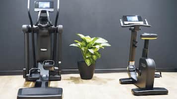 Two exercise machines and a potted plant in a room with a wooden floor and dark walls.