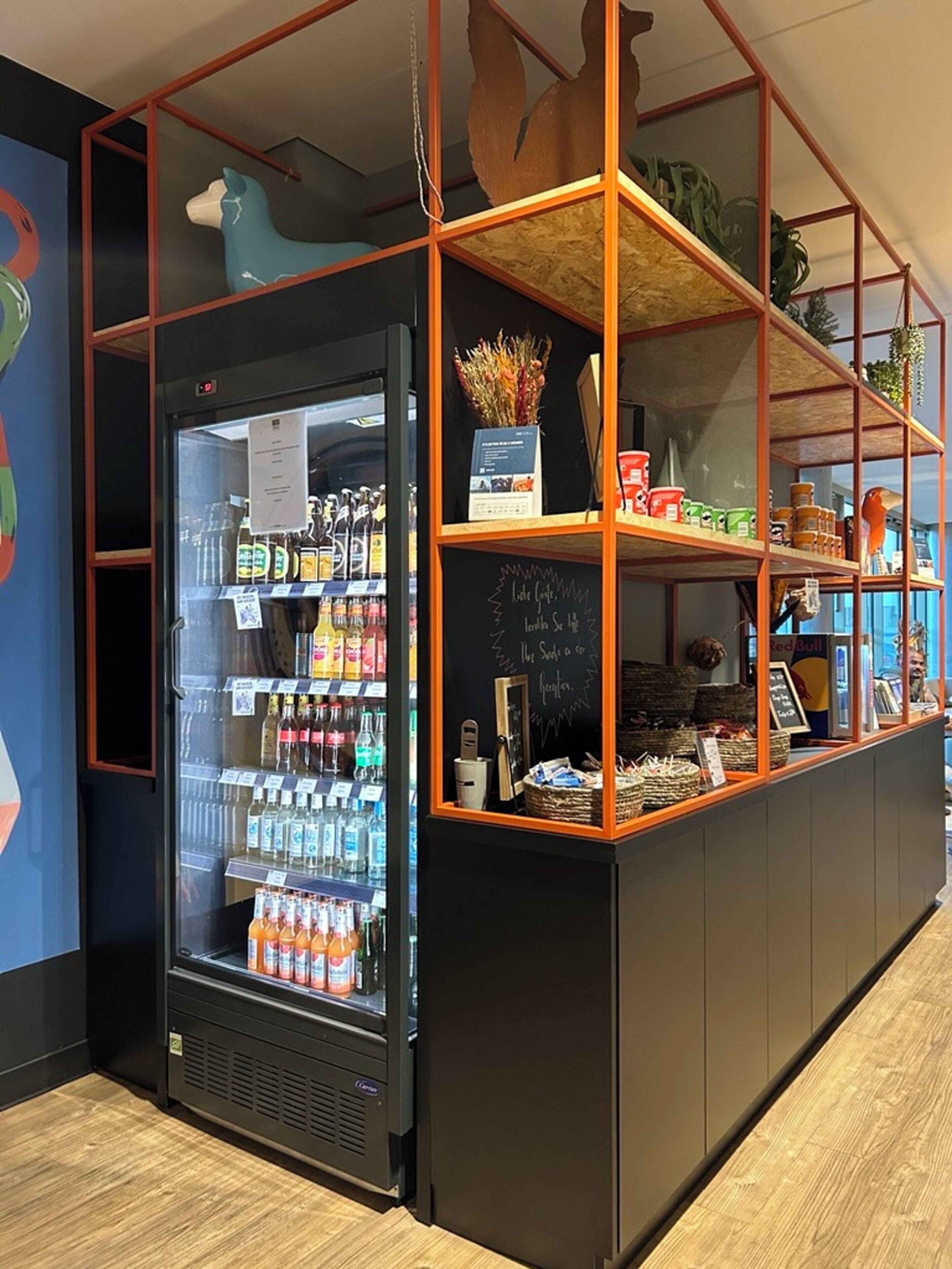 Ein Selbstbedienungsgetränkeautomat mit verschiedenen Getränken, einer Kreidetafel mit der Speisekarte und einem dekorativen Regal mit Gegenständen.