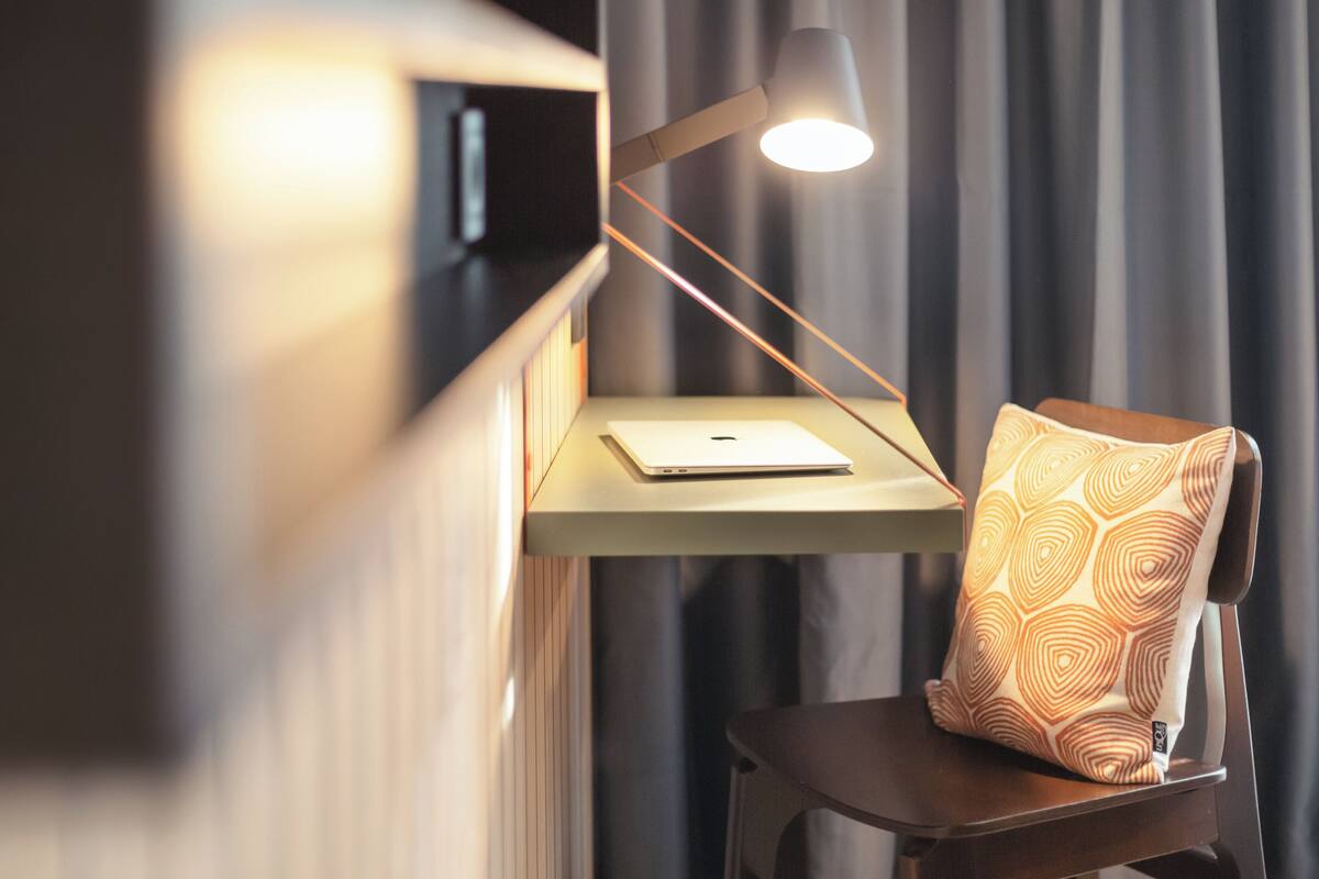 A modern room with a desk, a laptop, a patterned pillow, and a lamp.