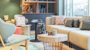 A cozy living room with a sofa, chairs, a round coffee table, and a bookshelf filled with books and decorative items. - Holiday Inn - the niu, Amity Potsdam by IHG (Potsdam)