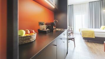 A modern hotel room with a kitchen area featuring a fruit bowl, coffee maker, and a sink.