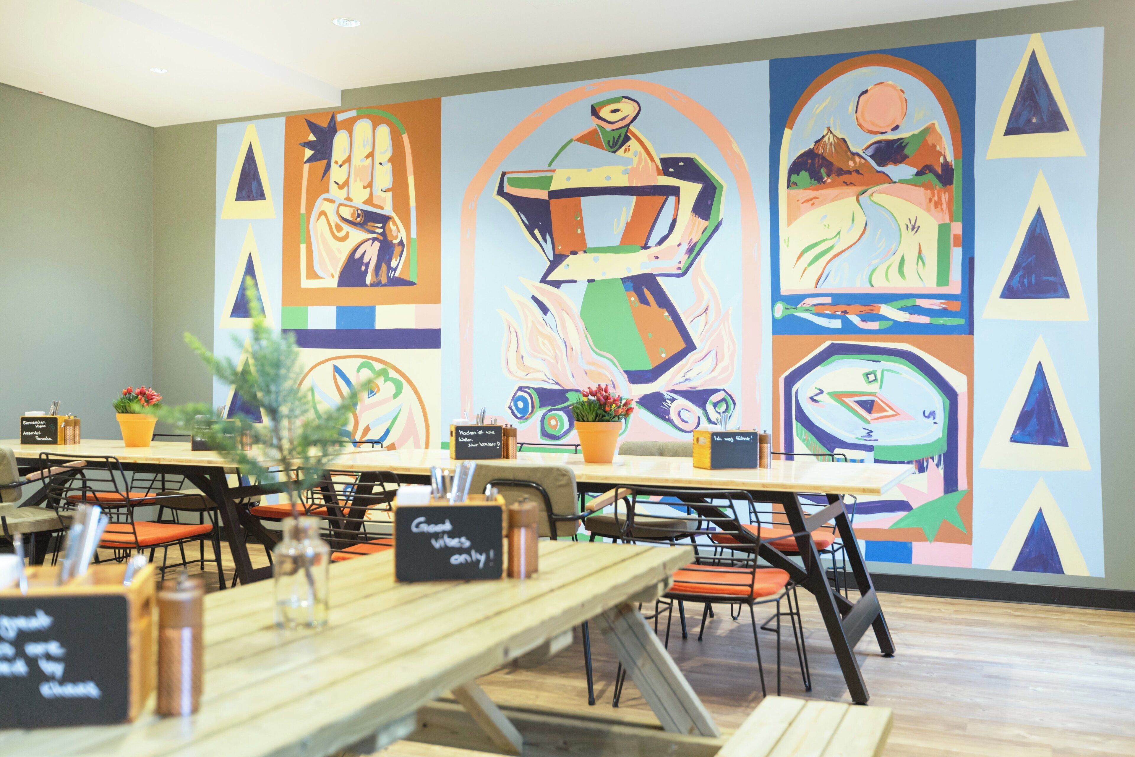 A restaurant with wooden tables and chairs, a colorful mural on the wall, and a sign that reads "Good vibes only!"