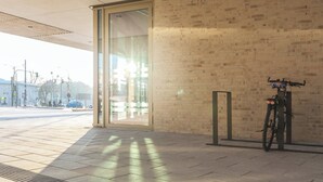 A building entrance with a glass door, a brick wall, and a bicycle parked outside. - Holiday Inn - the niu, Amity Potsdam by IHG (Potsdam)