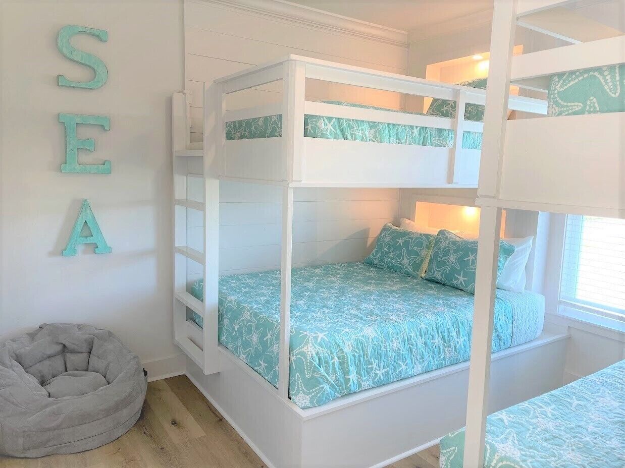 Une chambre avec un lit superposé, une couvre-lit sur le thème de la mer, un fauteuil en forme de poire de couleur grise et les lettres « SEA » peintes sur le mur.