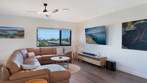 A modern living room with a leather sectional sofa, a round coffee table, a TV, and artwork on the walls. - Noble House - Absolutely Stunning House in Convenient Location! (Dalmeny)
