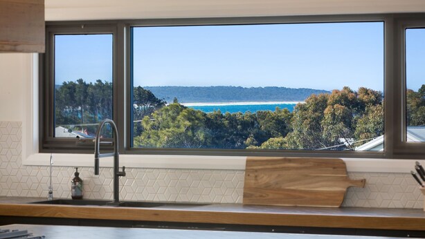 A kitchen with a large window overlooking a beach and forest. - Noble House - Absolutely Stunning House in Convenient Location! (Dalmeny)