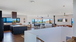 A modern kitchen with a large island, dining area with a view, and a living area with a fireplace. - Noble House - Absolutely Stunning House in Convenient Location! (Dalmeny)