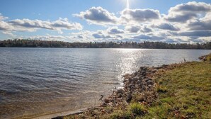 Um lago com águas cristalinas, uma margem rochosa e uma linha de árvores ao longe, sob um céu parcialmente nublado.