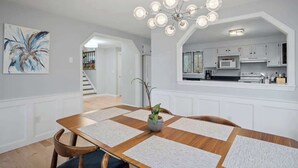 Uma área de refeições com mesa de madeira, cadeiras, uma planta central e um lustre moderno.