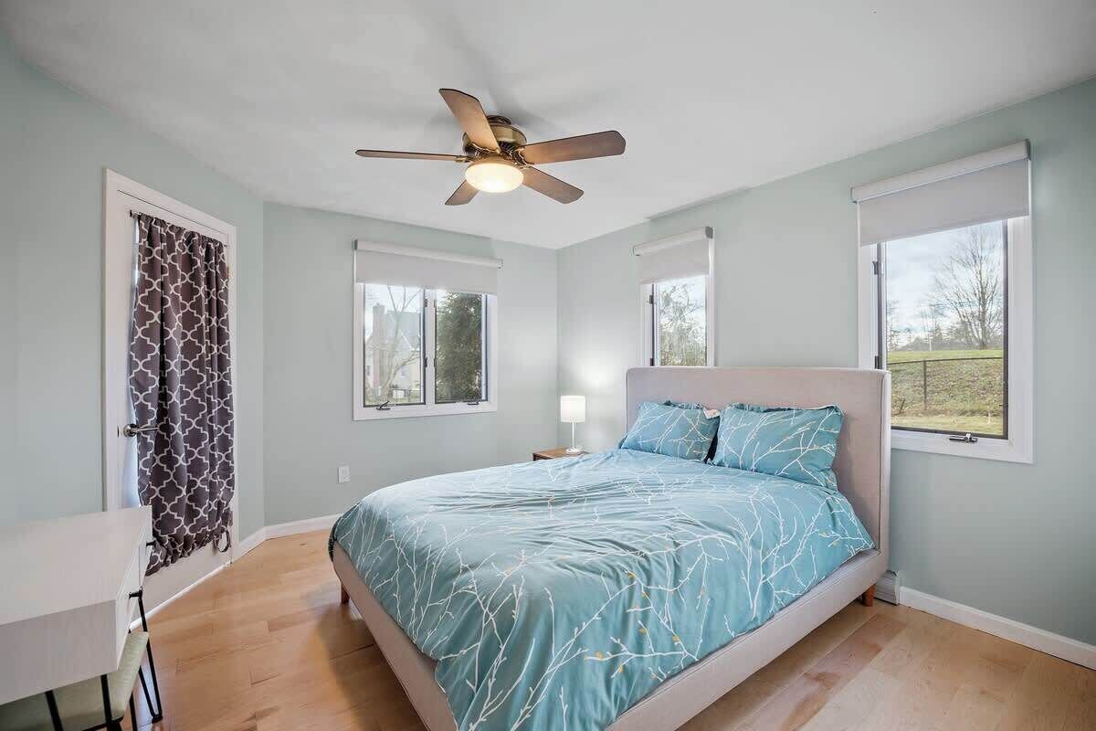 Un dormitorio con cama, ventilador de techo, escritorio y ventana.