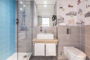 A bathroom with a glass-enclosed shower, a wooden vanity with a sink, and a toilet. - Holiday Inn - the niu, Yen Hamburg City by IHG (Hamburg)