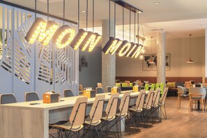 A modern dining area with a long table, chairs, and hanging light fixtures spelling out "MOM". - Holiday Inn - the niu, Yen Hamburg City by IHG (Hamburg)