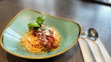 Une assiette de spaghettis à la sauce tomate, garnie d’une feuille de basilic, le tout présenté dans une assiette en céramique.