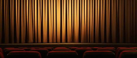 Un teatro con hileras de asientos rojos y un gran telón.