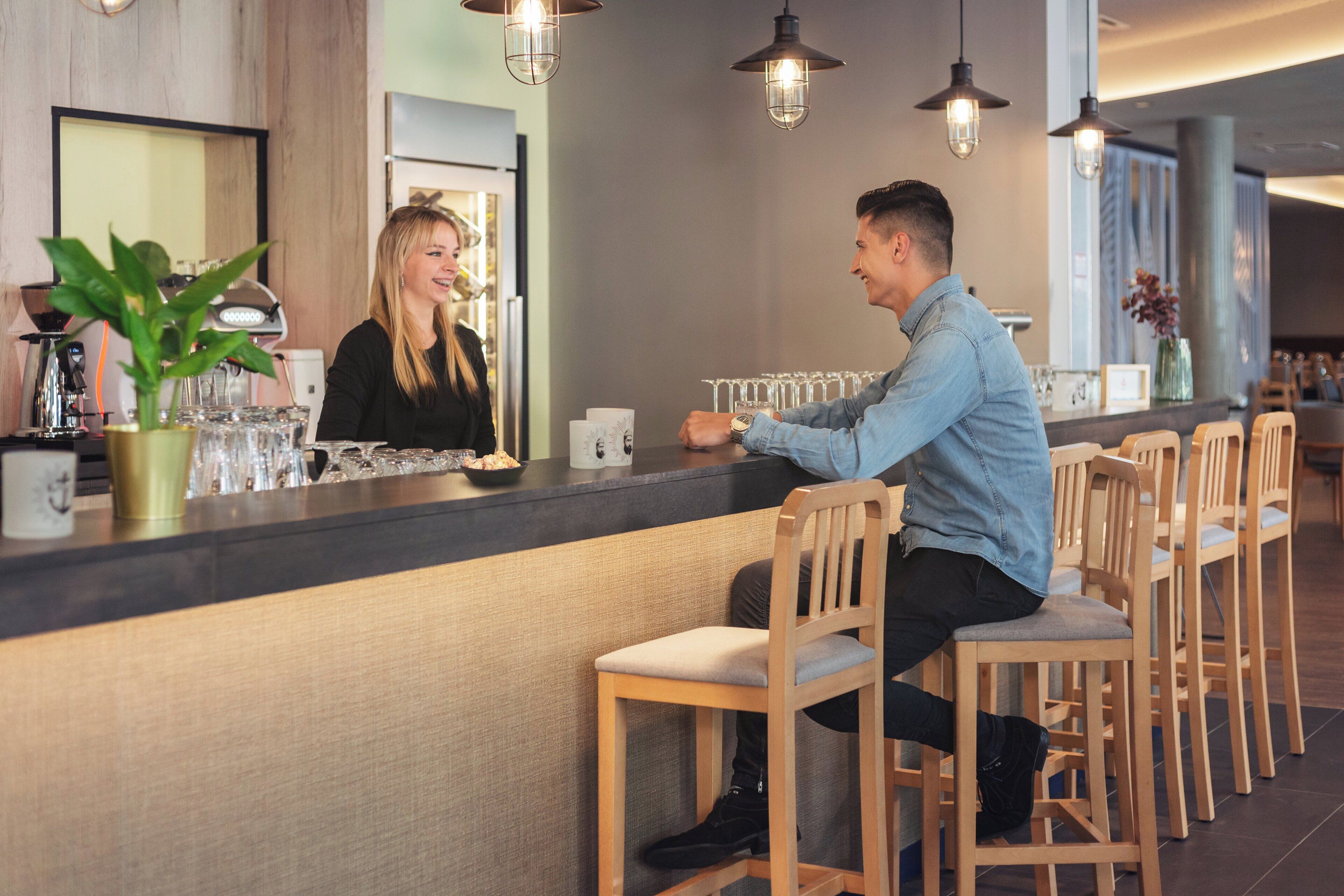 A bar area with wooden chairs, a counter with a glass display, and hanging pendant lights.