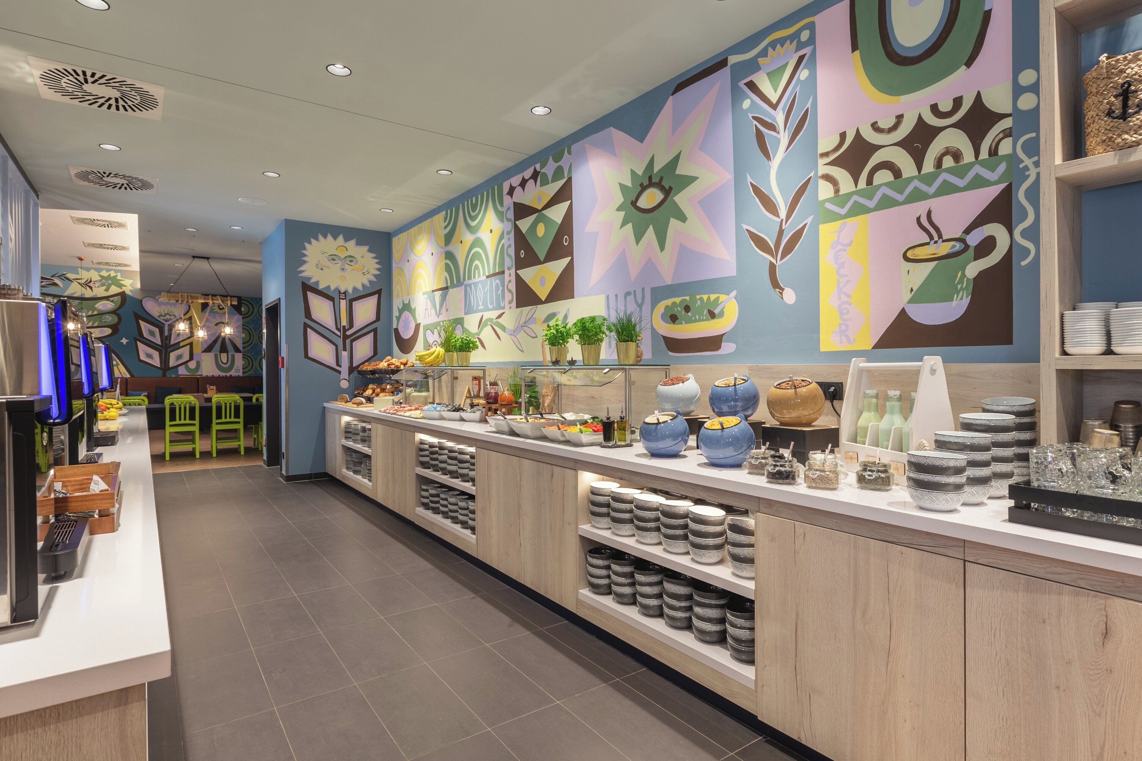 Una cafetería moderna con una barra alargada, estantes con cuencos y un mural colorido en la pared.