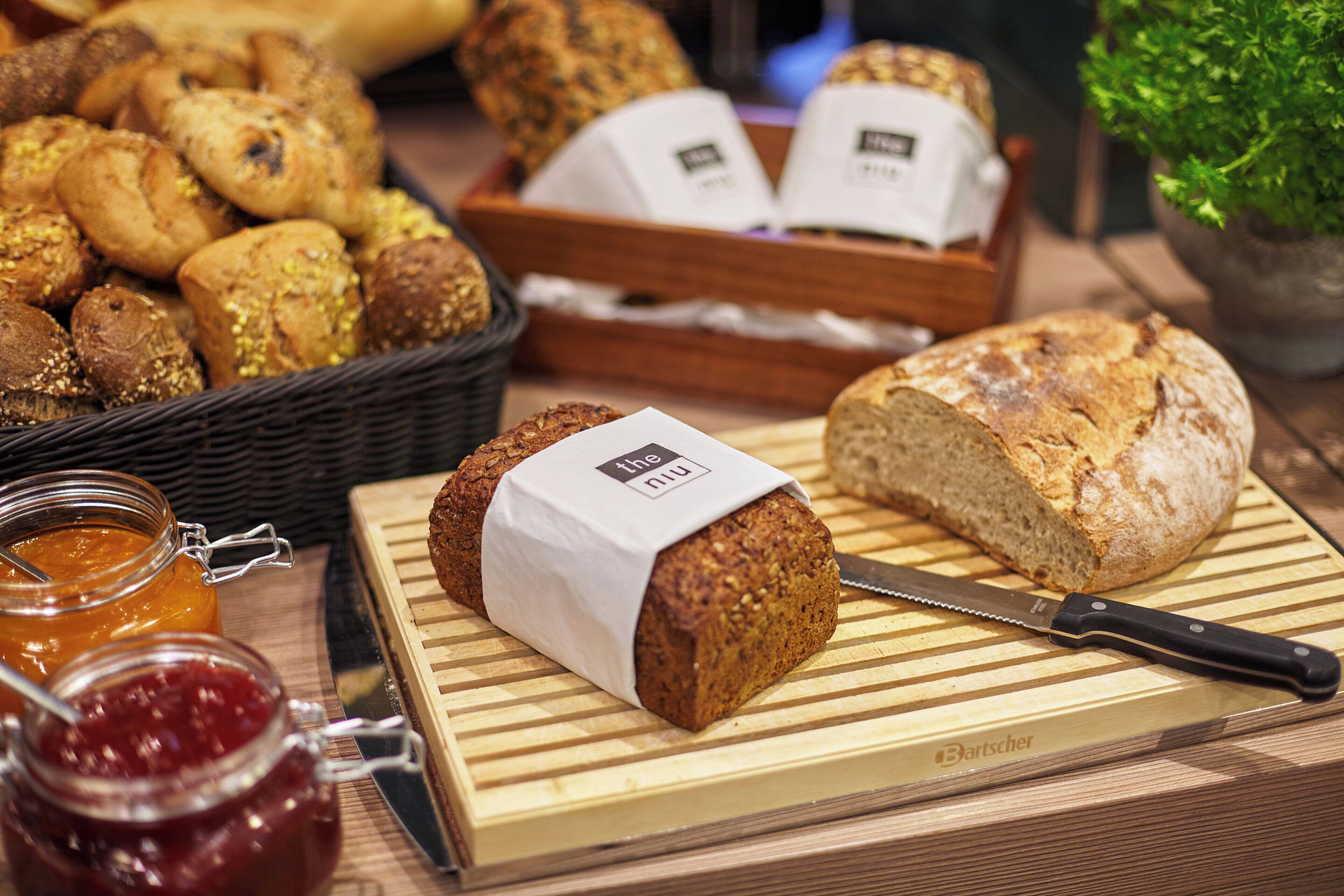 Verschiedene Brotsorten und Gebäck auf einem Holztisch, darunter ein Brot mit einem Etikett und einem Messer.