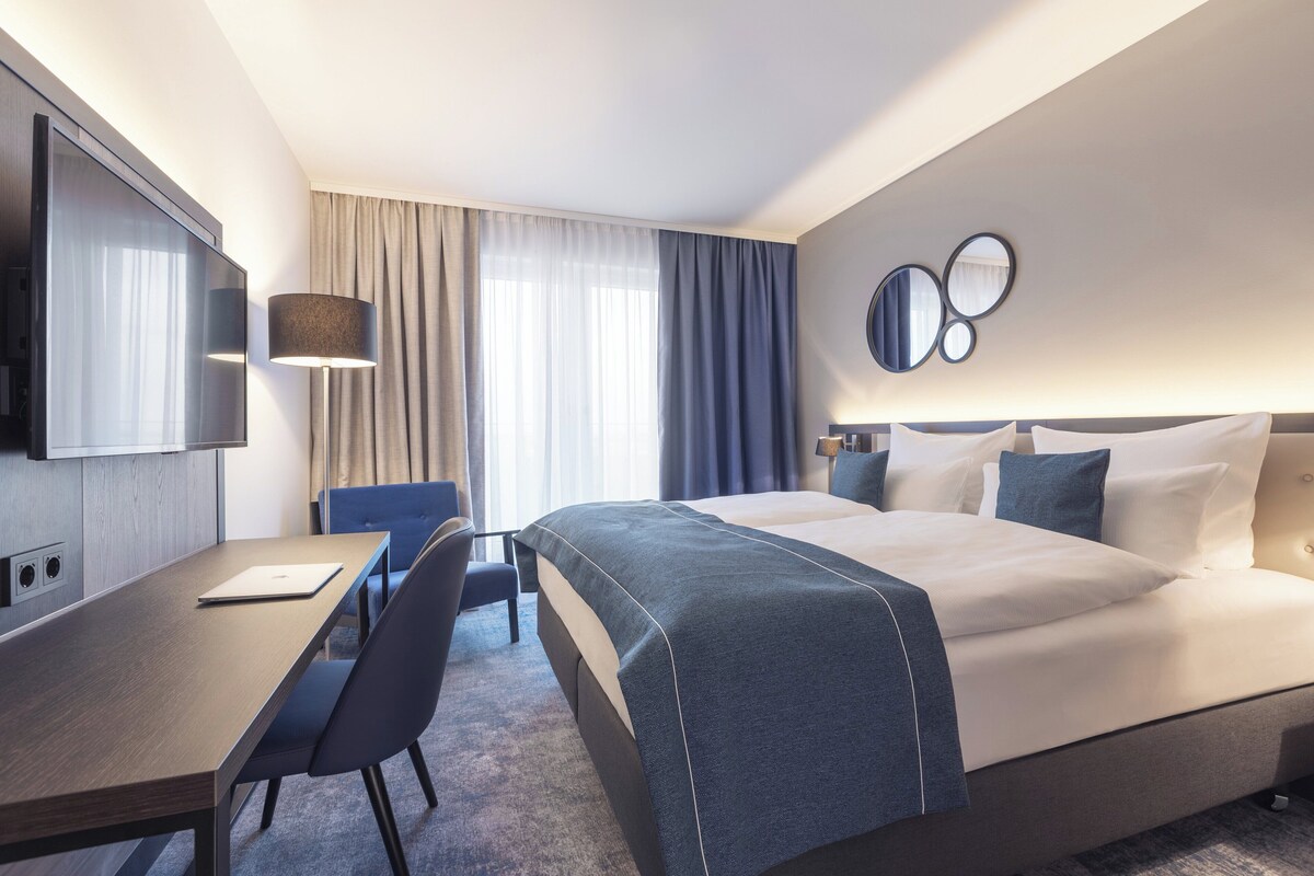 Habitación de hotel con cama, escritorio, silla, televisor y un muro con espejos circulares.