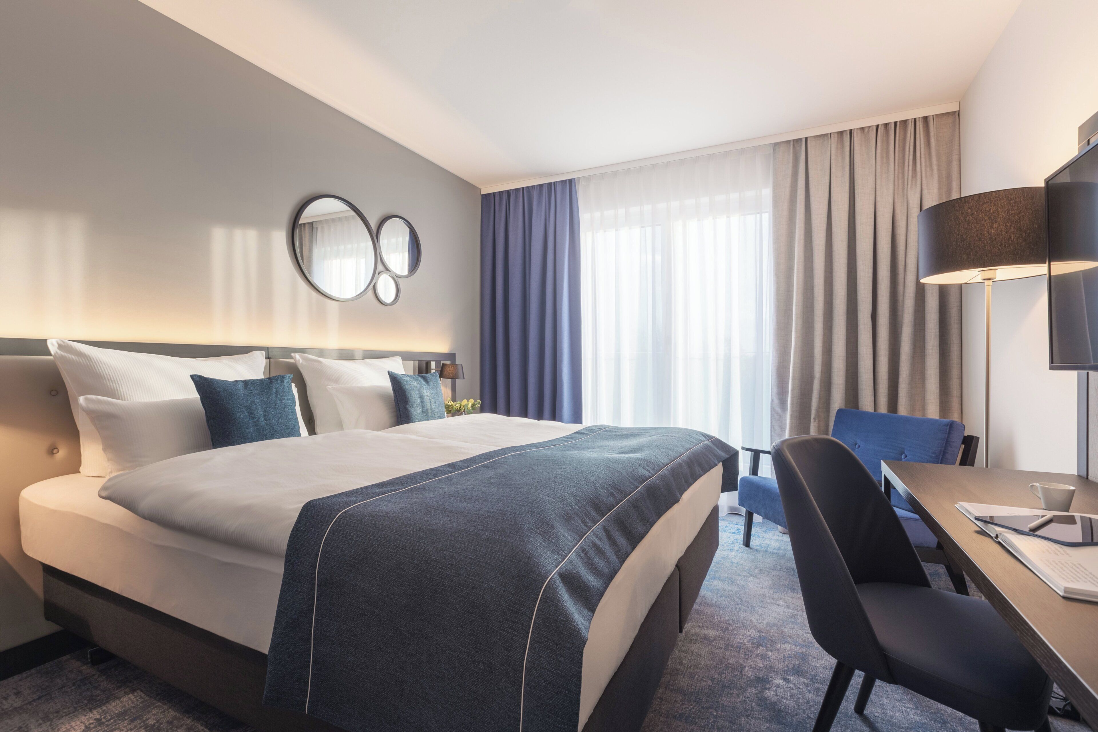 Habitación de hotel con una cama grande, un escritorio con una silla, una lámpara y un televisor.