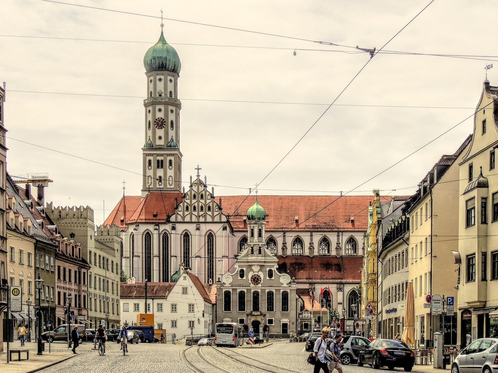 A historic building with a prominent tower and a green dome, surrounded by cobblestone streets and classic architecture.