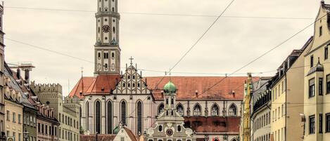 A historic building with a prominent tower and a green dome, surrounded by cobblestone streets and classic architecture.