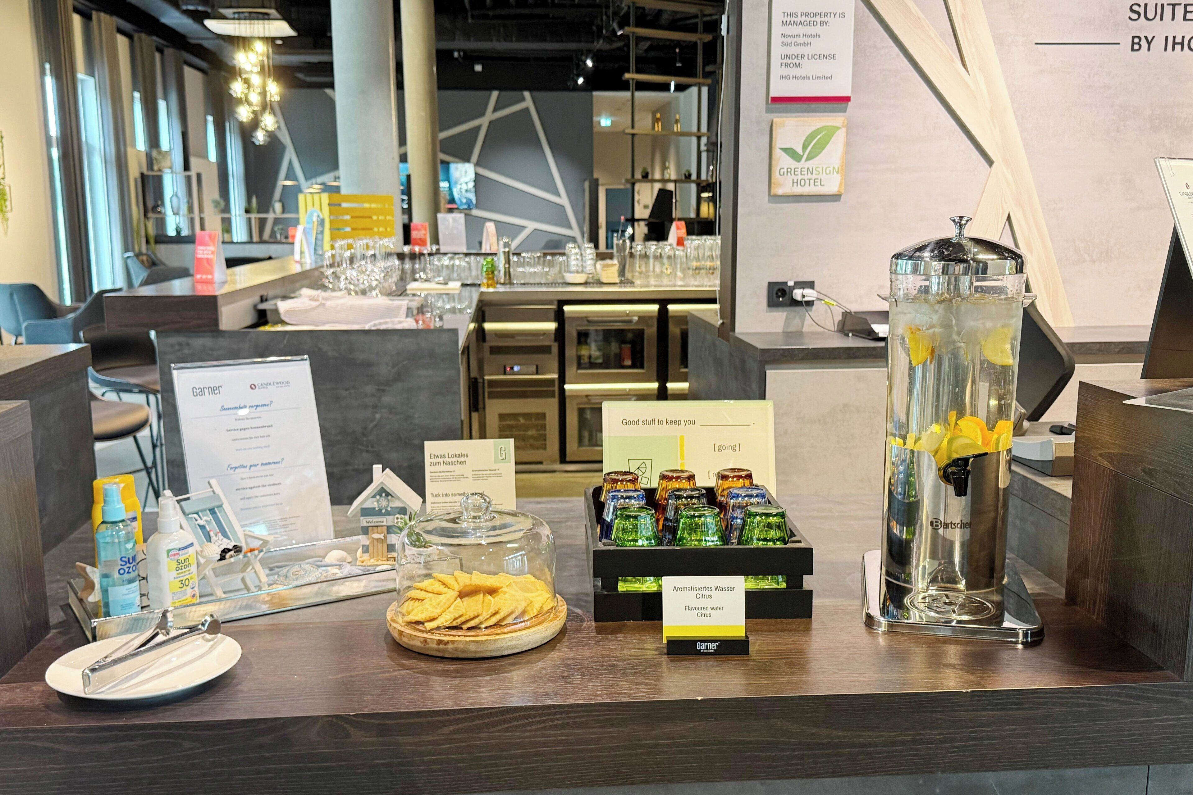 A hotel reception area with a counter displaying amenities like glasses, a water dispenser, and a tray with snacks.
