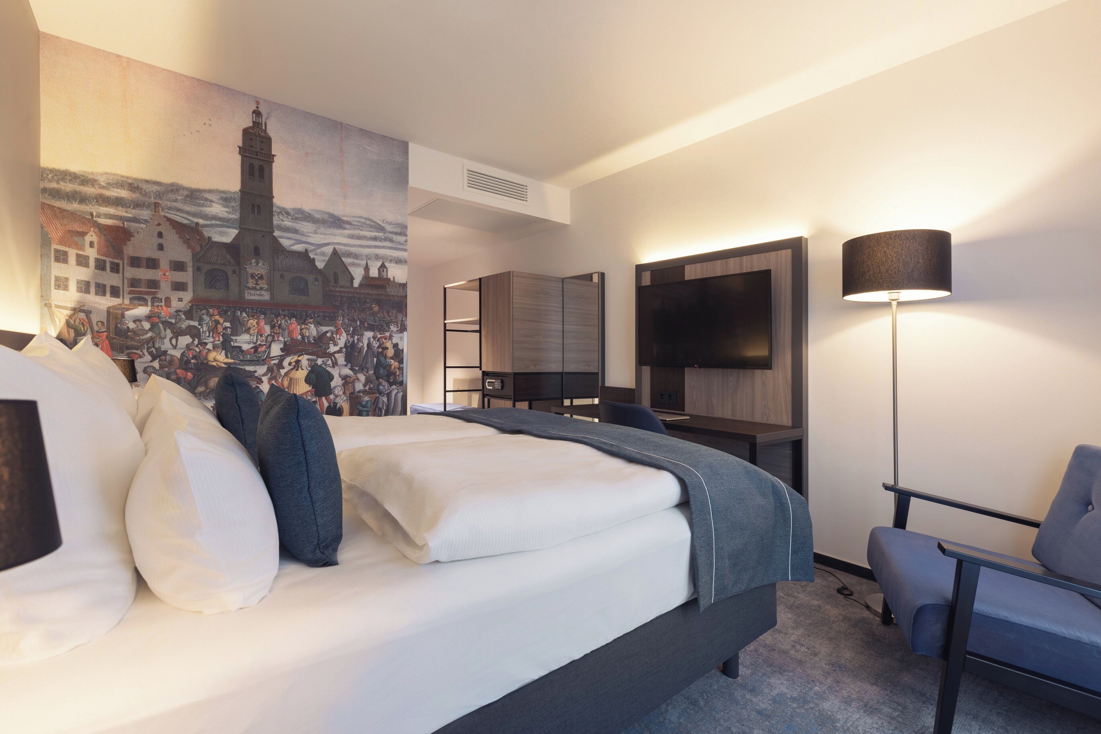 Habitación de hotel con cama, escritorio, silla, televisión y un cuadro en la pared.