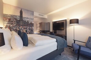 Habitación de hotel con cama, escritorio, silla, televisión y un cuadro en la pared.