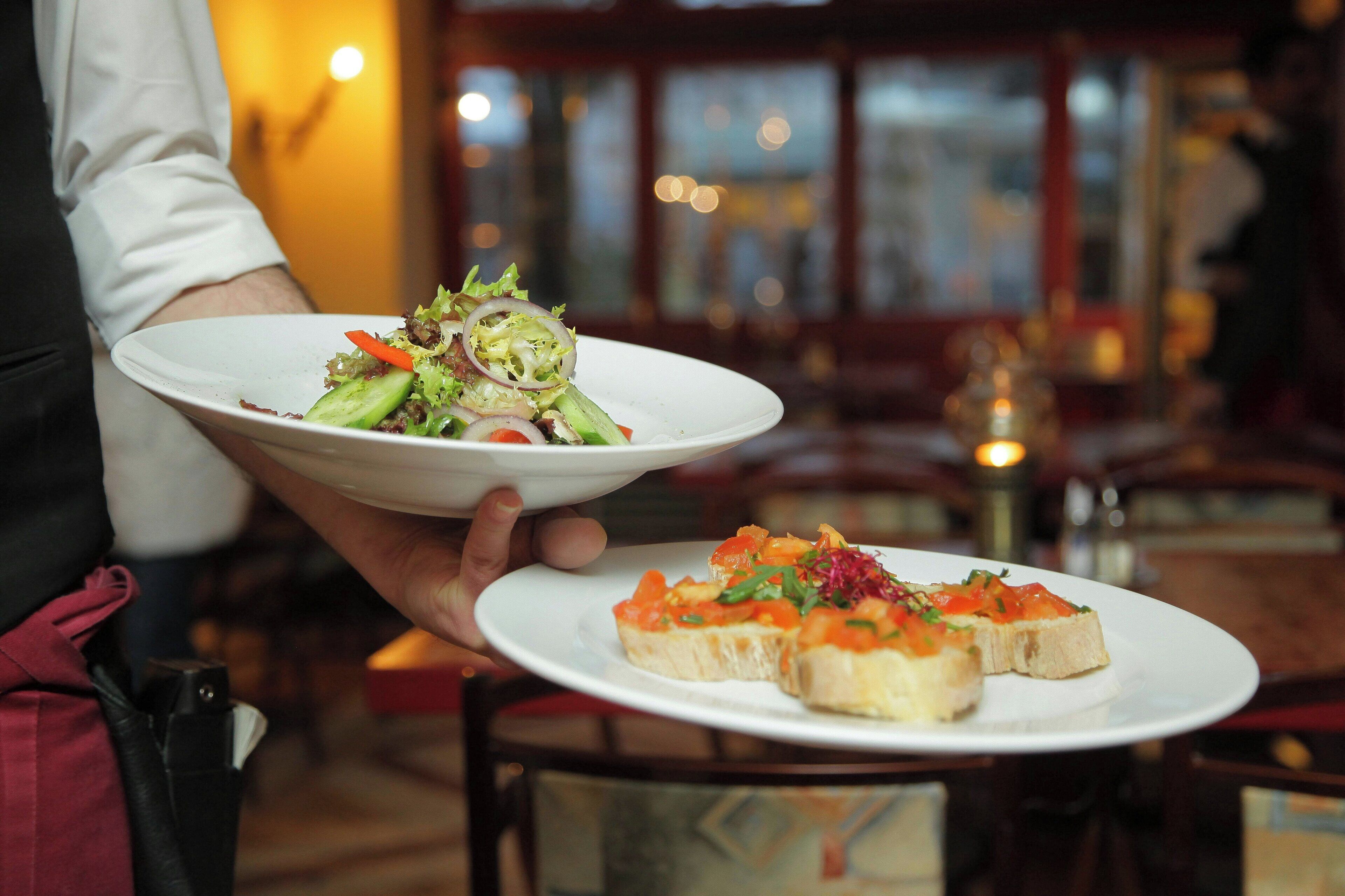 Une personne tenant deux assiettes, l’une contenant une salade et l’autre des bruschettas.