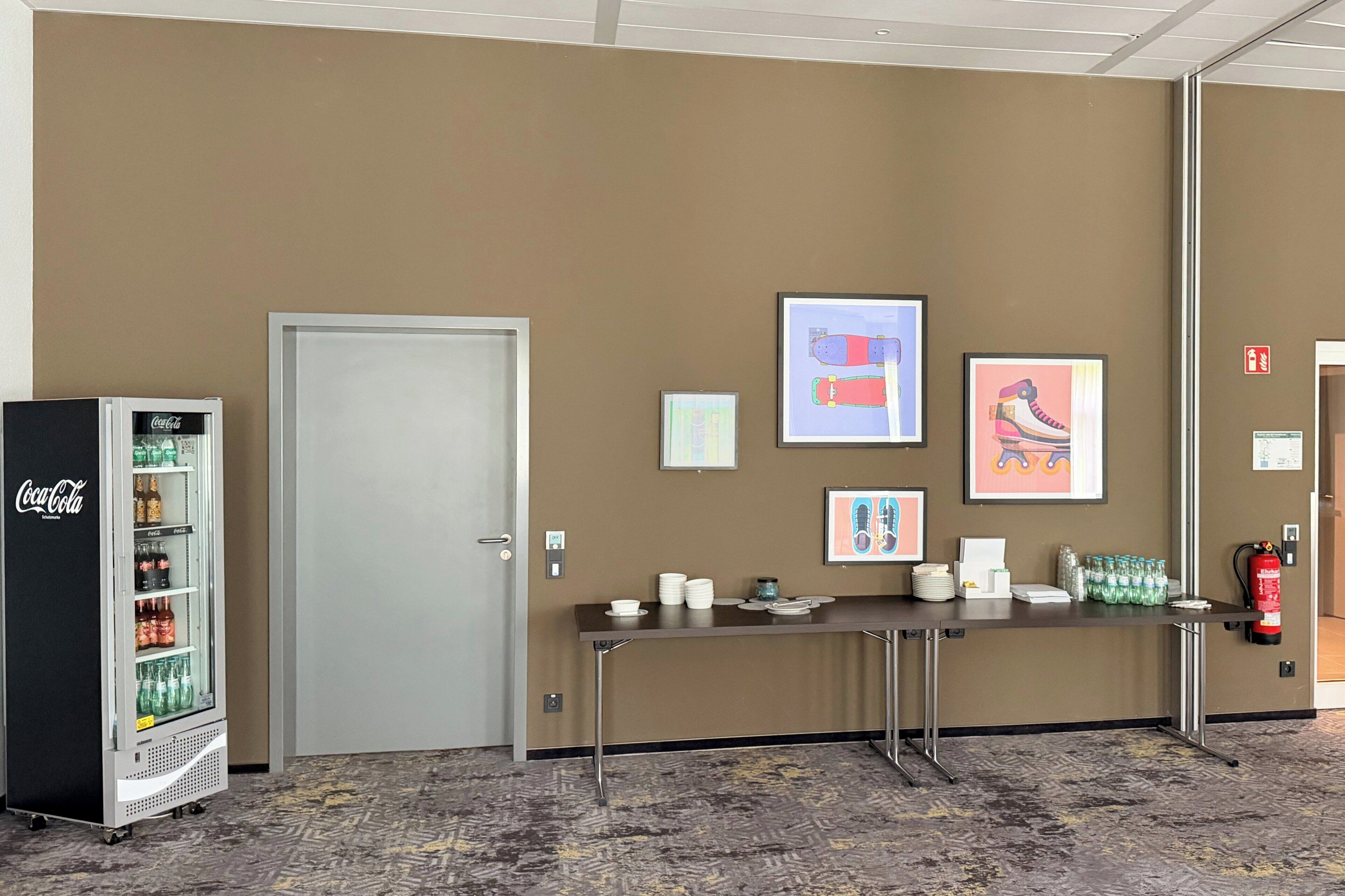 A lobby with a Coca-Cola refrigerator, a reception desk, framed artwork on the wall, and a fire extinguisher.