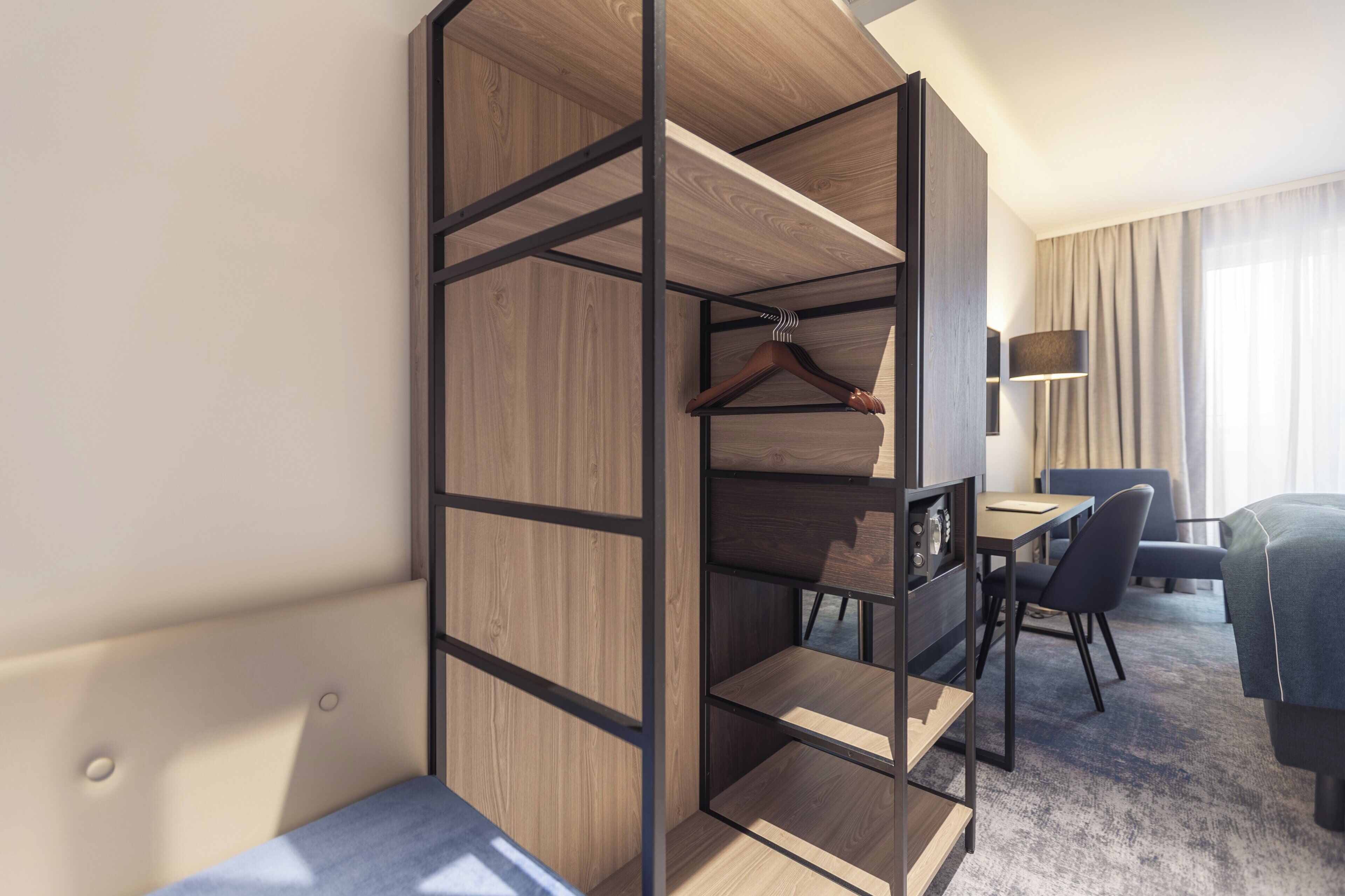 A modern hotel room with a wooden wardrobe, a desk with a chair, and a sofa.