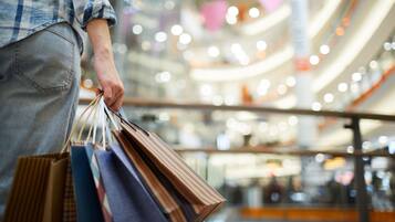 A person holding shopping bags in a brightly lit indoor space with a modern architectural design.