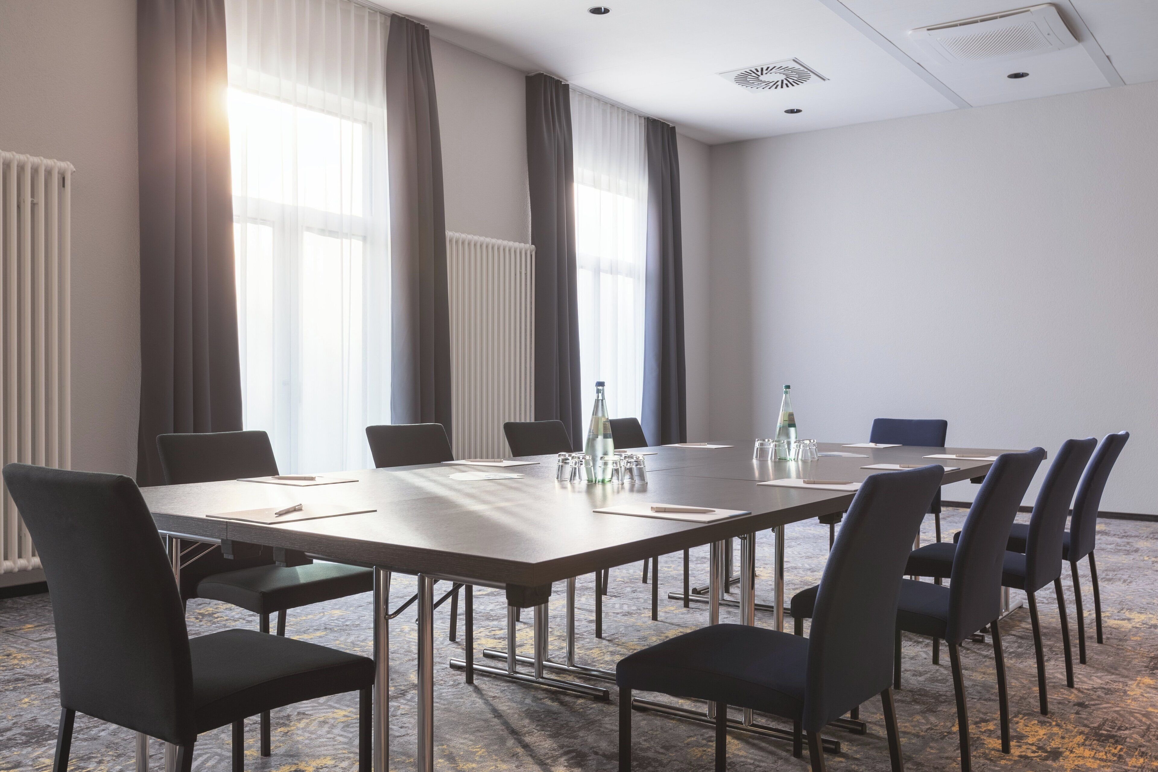 Un salón de conferencias con una larga mesa, sillas y una botella de agua.
