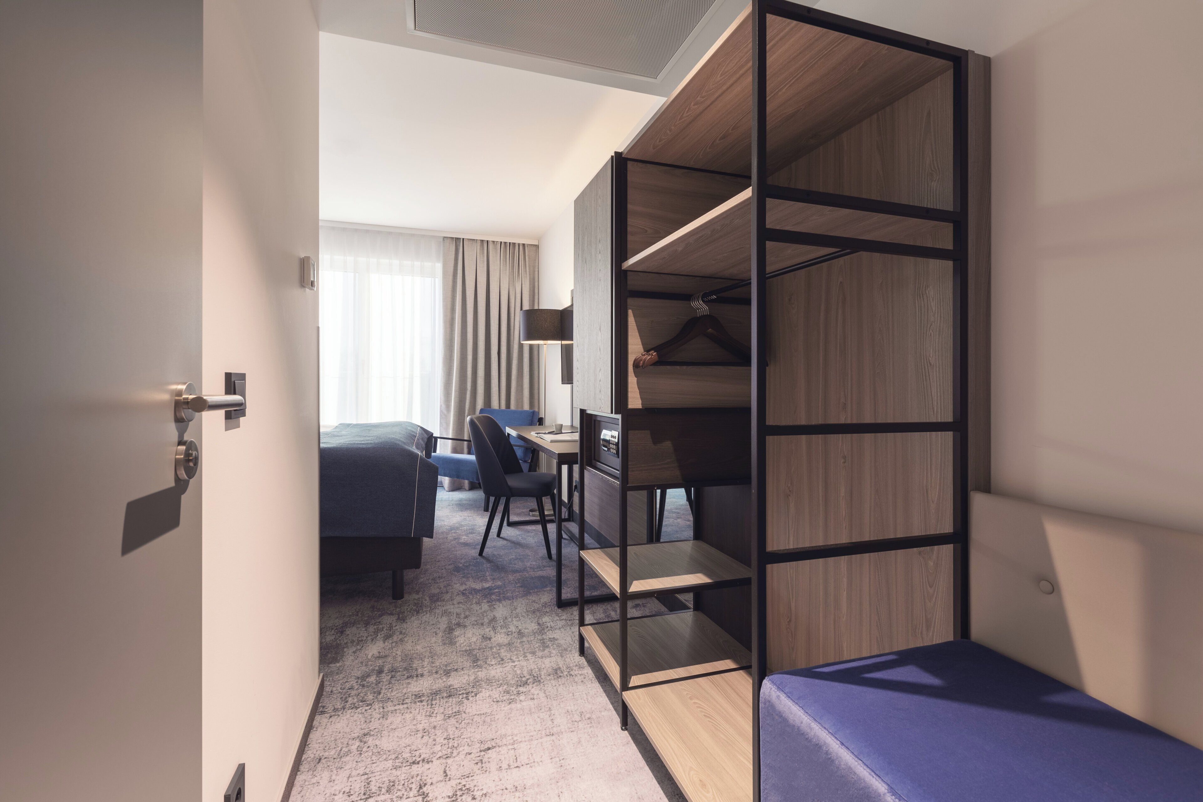Una habitación de hotel moderna con cama, escritorio, silla y armario con estantes.