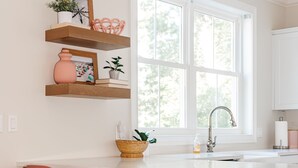 A kitchen with wooden bar stools, a white countertop, and a window with a view of trees.