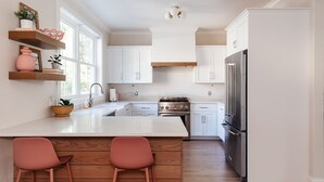 A modern kitchen with white cabinets, a stainless steel refrigerator, and a central island with two pink chairs.